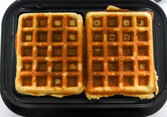 Two waffles cooking on a waffle iron.
