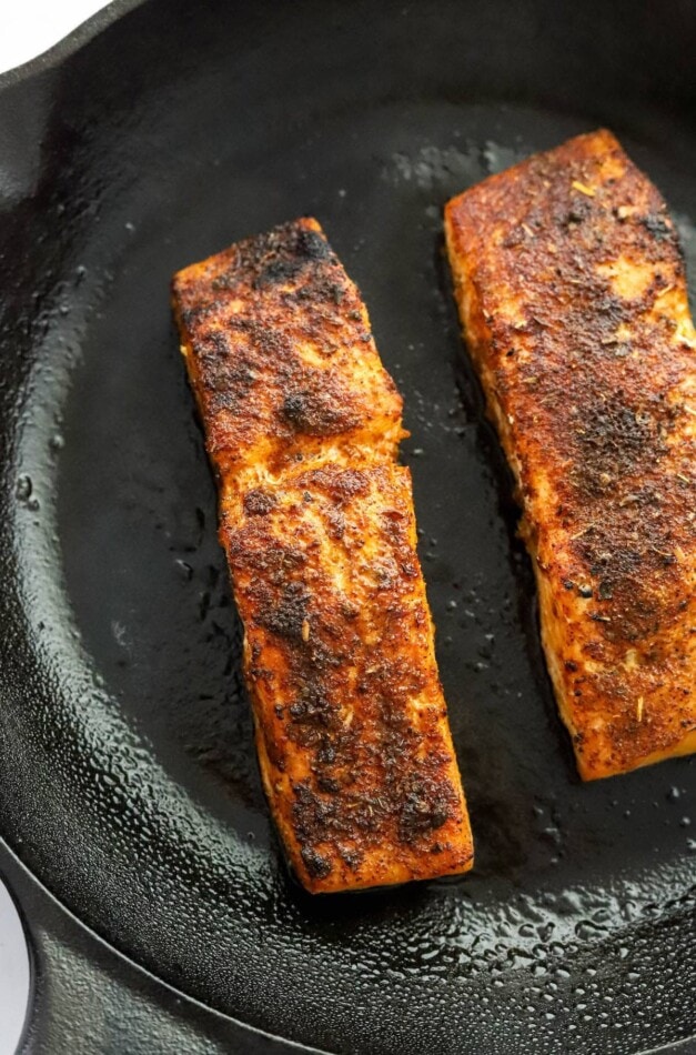 Two salmon filets cooking in a cast iron skillet.