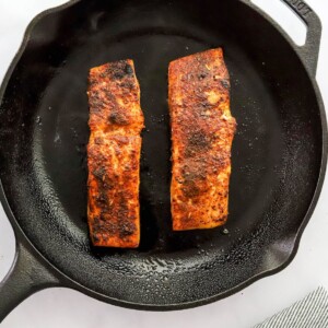 Two salmon filets cooking in a cast iron skillet.