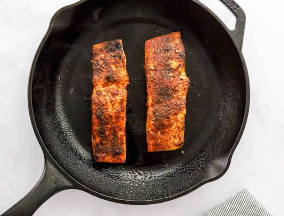 Two salmon filets cooking in a cast iron skillet.