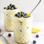 Two mason jars containing blueberry lemon overnight oats. The jars are topped with blueberries and lemon zest.