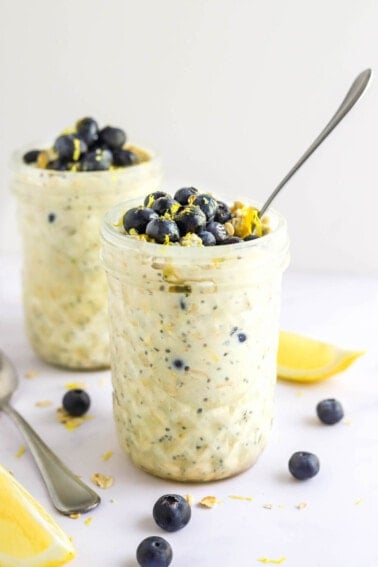 Two mason jars containing blueberry lemon overnight oats. The jars are topped with blueberries and lemon zest.