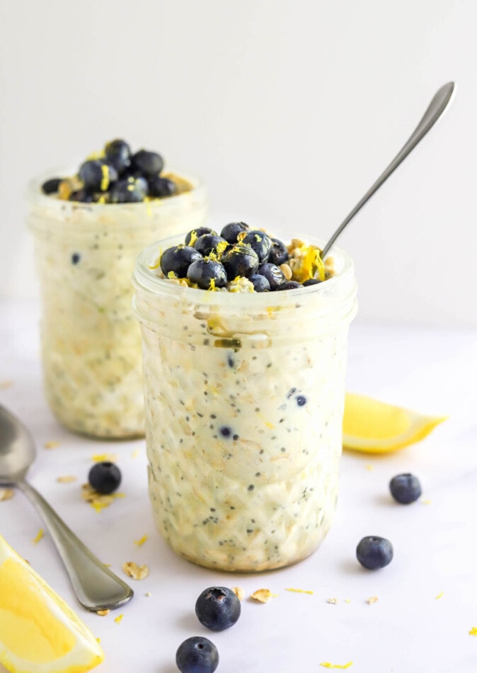 Two mason jars containing blueberry lemon overnight oats. The jars are topped with blueberries and lemon zest.