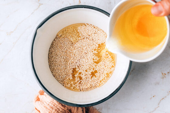 Pouring vegetable broth into pot containing dry quinoa.