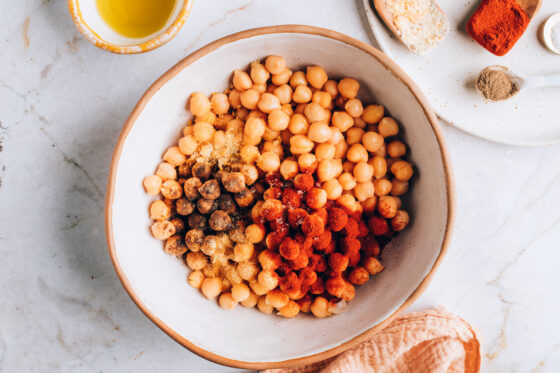 A bowl of chickpeas. Spices are being added to the bowl.