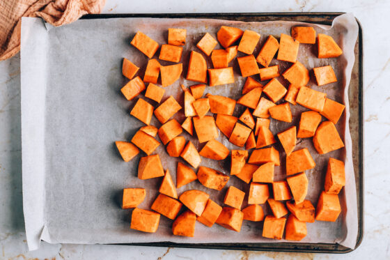A sheet pan lined in parchment paper. Two thirds of the sheet pan is covered by chunks of sweet potato.
