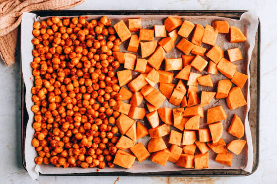 A sheet pan lined in parchment paper. Two thirds of the sheet pan is covered by chunks of sweet potato and one third is covered with chickpeas.