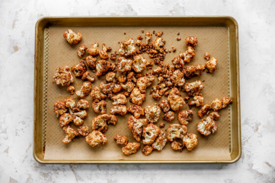 Cauliflower florets tossed in taco seasoning, spread across a sheet pan lined with parchment paper.