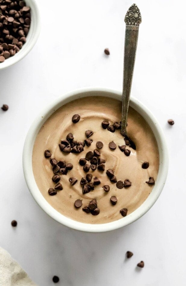 A small dish containing chocolate protein pudding topped with chocolate chips. A spoon rests in the bowl.