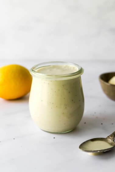 A small tulip jar containing caesar salad dressing. A small spoon rests next to the jar.