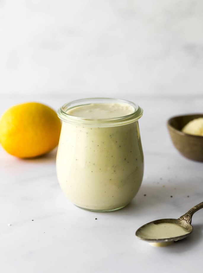 A small tulip jar containing caesar salad dressing. A small spoon rests next to the jar.