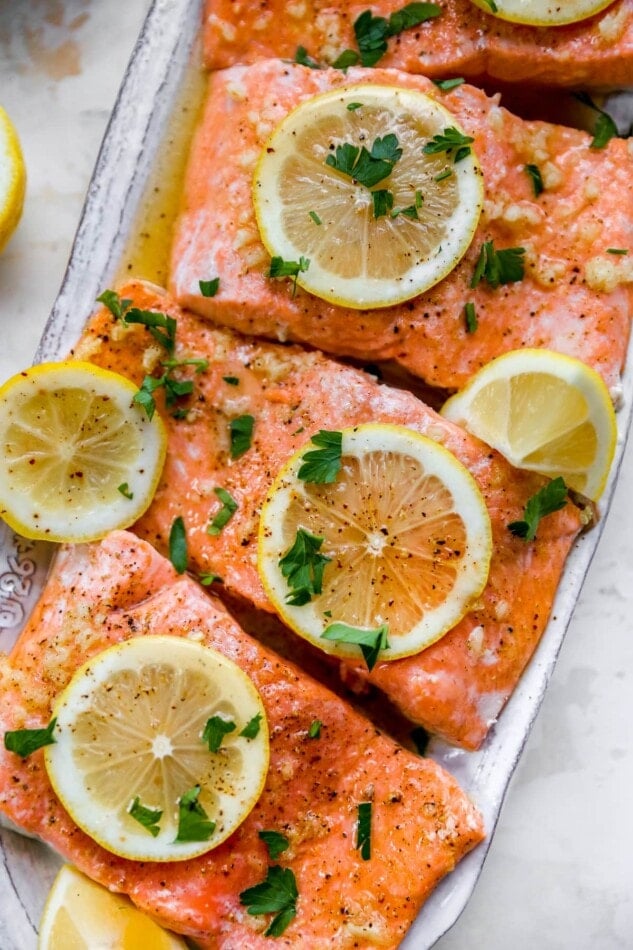 A closeup of 3 salmon filets garnished with lemon slices and fresh garlic.