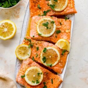 Honey Lemon Garlic salmon filets on a plate garnished with lemon slices and parsley.