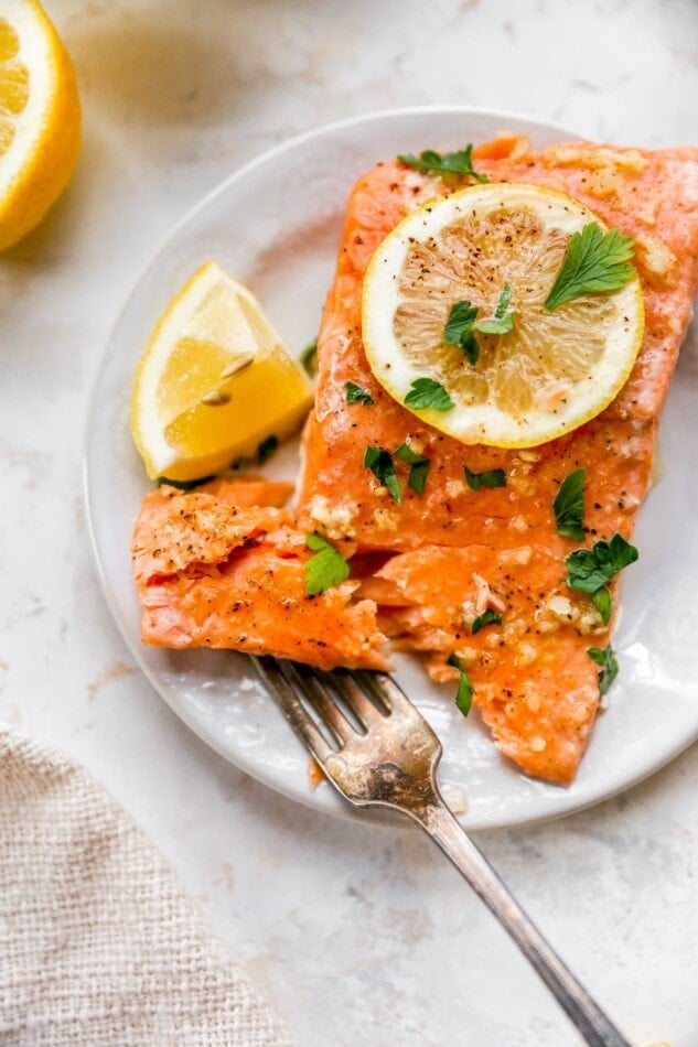 A filet of salmon on a plate. A fork has a bite removed from the filet.