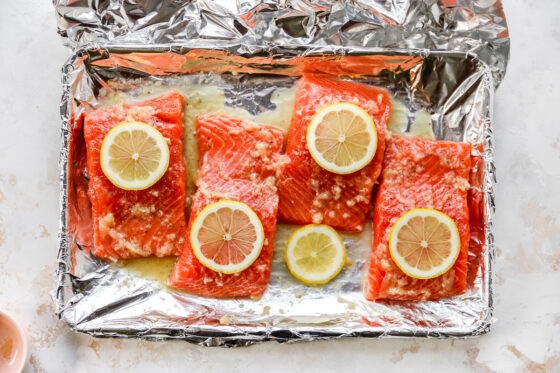 Four salmon filets covered in honey lemon garlic butter and topped with lemon slices.