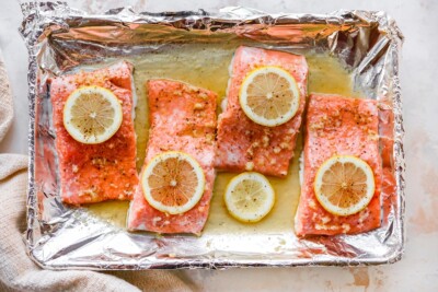 Four filets of baked honey lemon garlic salmon on a baking sheet lined in foil.