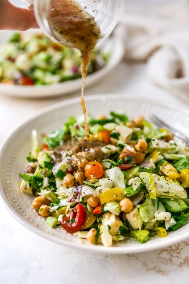 Drizzling dressing onto a plate containing Italian chopped salad.