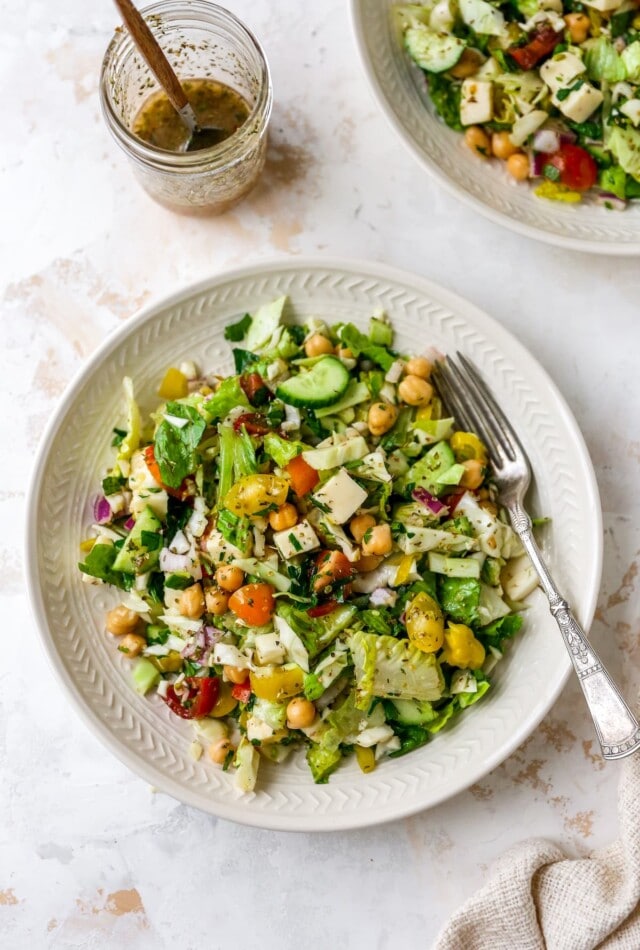 Overhead view of a plate containing Italian chopped salad. A jar containing dressing is resting next to the plate.