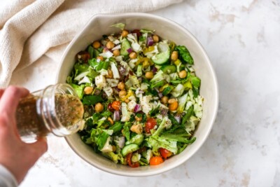 Drizzling dressing over Italian chopped salad ingredients in a bowl.