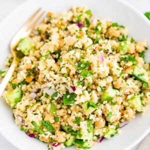 Quinoa salad on a white plate with a gold fork.