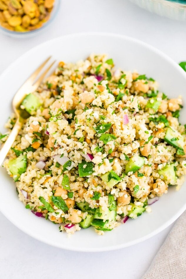 Quinoa salad on a white plate with a gold fork.