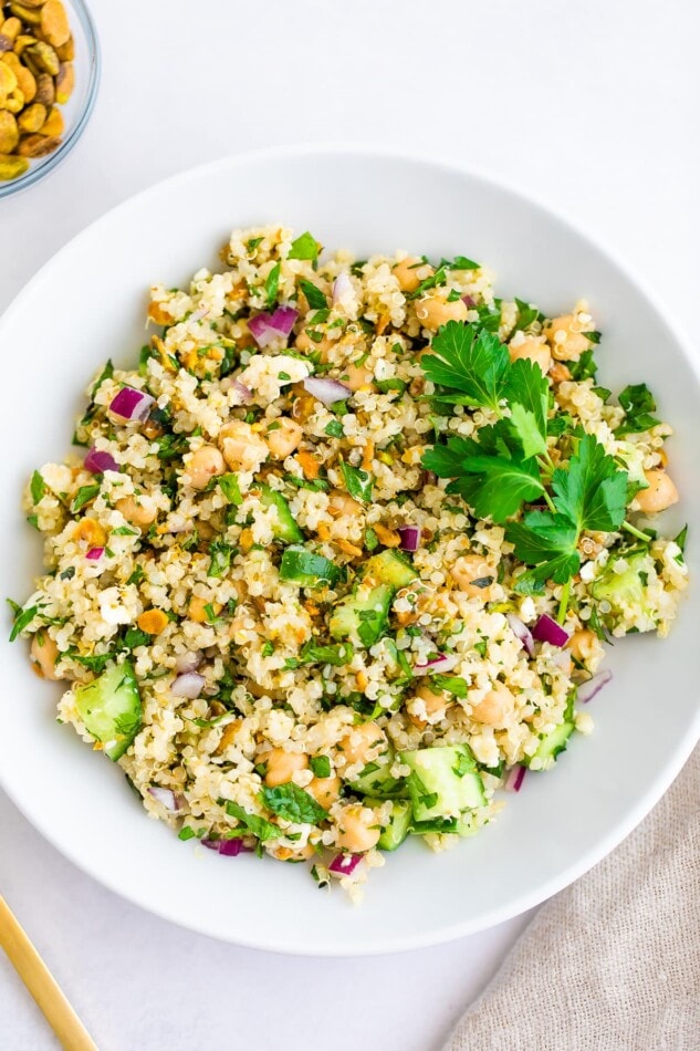 Quinoa salad in a white bowl with a parsley garnish.