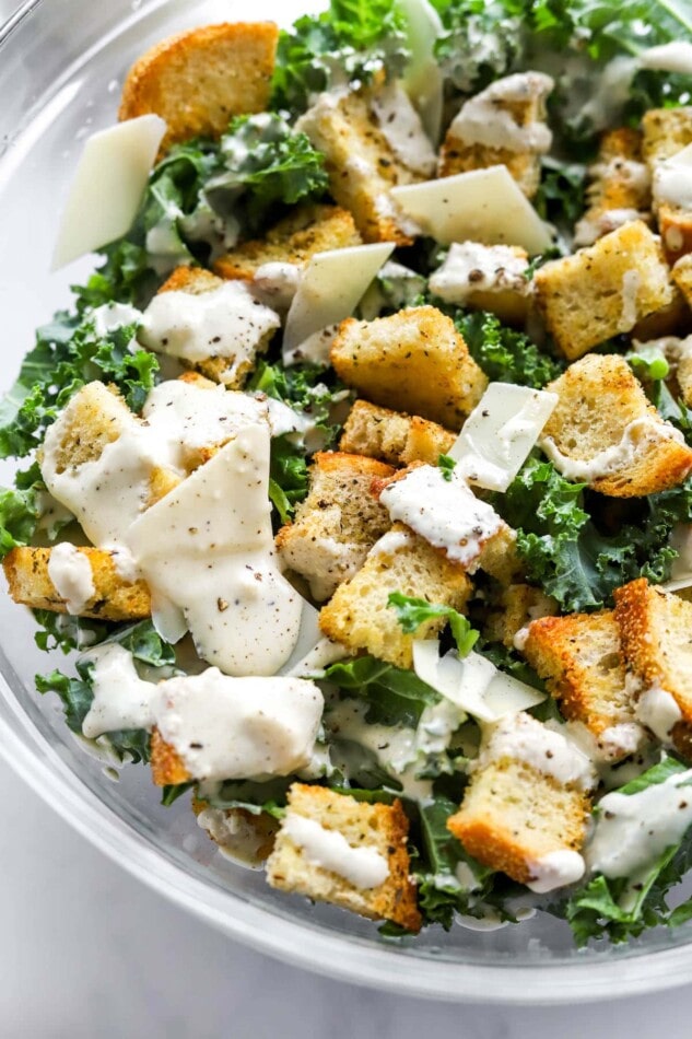 Closeup photo of kale salad topped with sourdough croutons, parmesan cheese and healthy caesar dressing.
