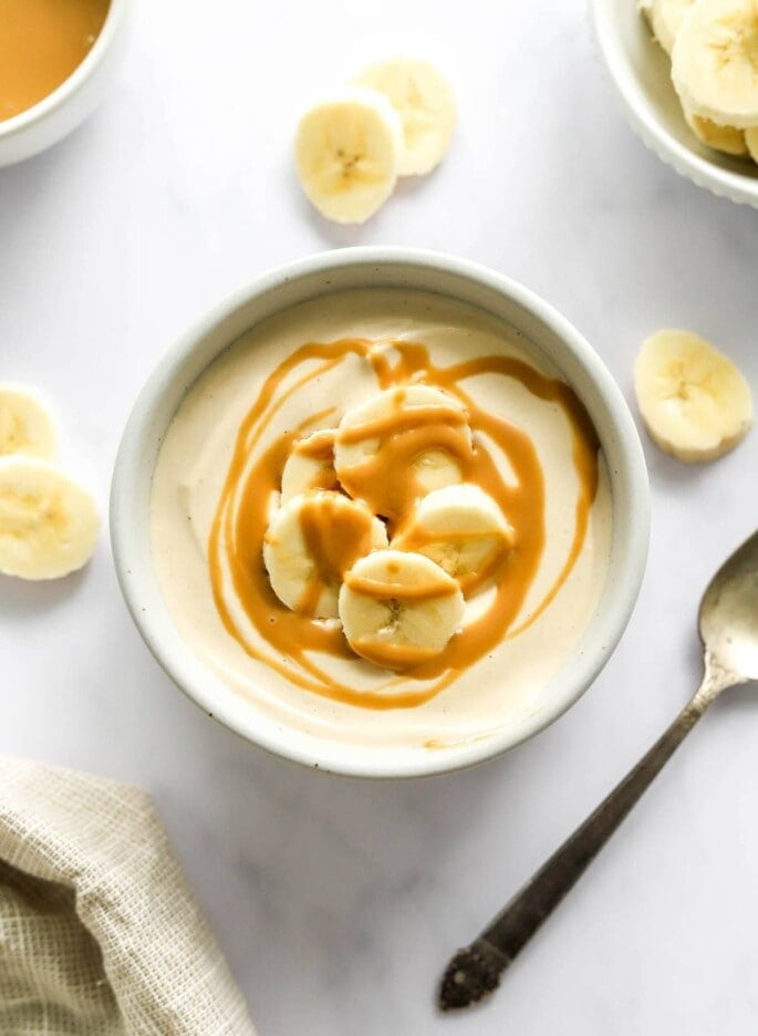 A small dish containing peanut butter protein pudding topped with banana slices and peanut butter drizzle.