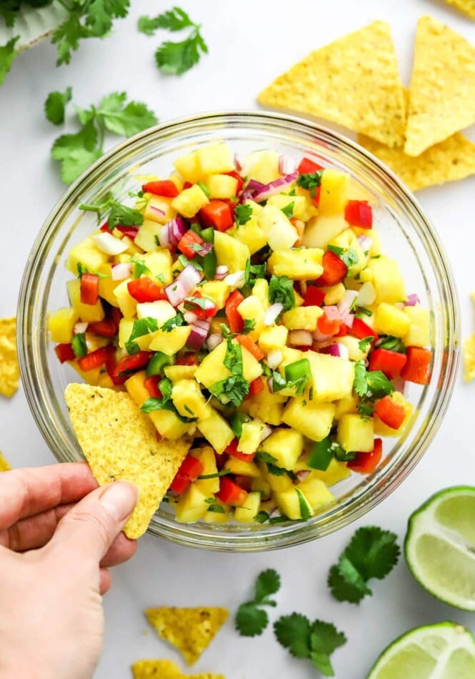 A hand scooping a bite of pineapple salsa onto a chip.