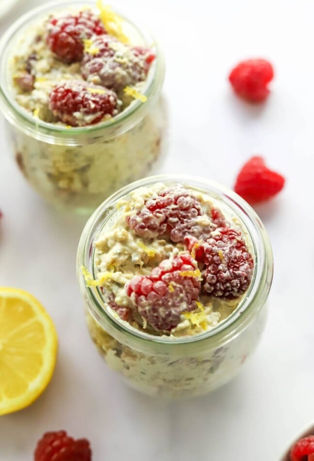 Two jars of raspberry lemon overnight oats topped with raspberries and lemon zest.