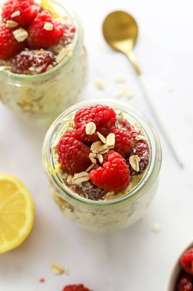 Overhead view of a jar of raspberry lemon overnight oats topped with additional raspberries. A spoon rests on the counter and a second jar is in the background.