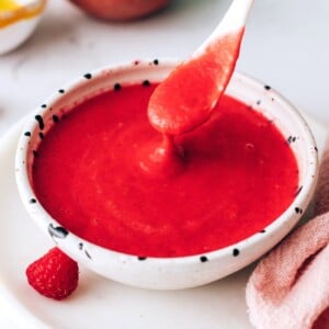 A small serving dish filled with raspberry vinaigrette. A spoon is lifting some out of the bowl.