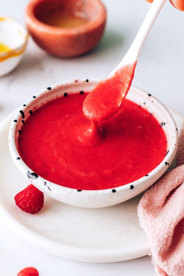 A small serving dish filled with raspberry vinaigrette. A spoon is lifting some out of the bowl.