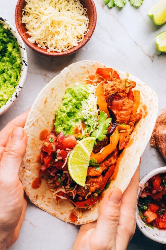 A chicken fajita being folded by two hands.