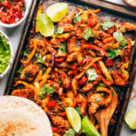 Chicken fajita filling on a sheet pan with a wooden spoon. Tortillas are resting on the bottom of the sheet pan.