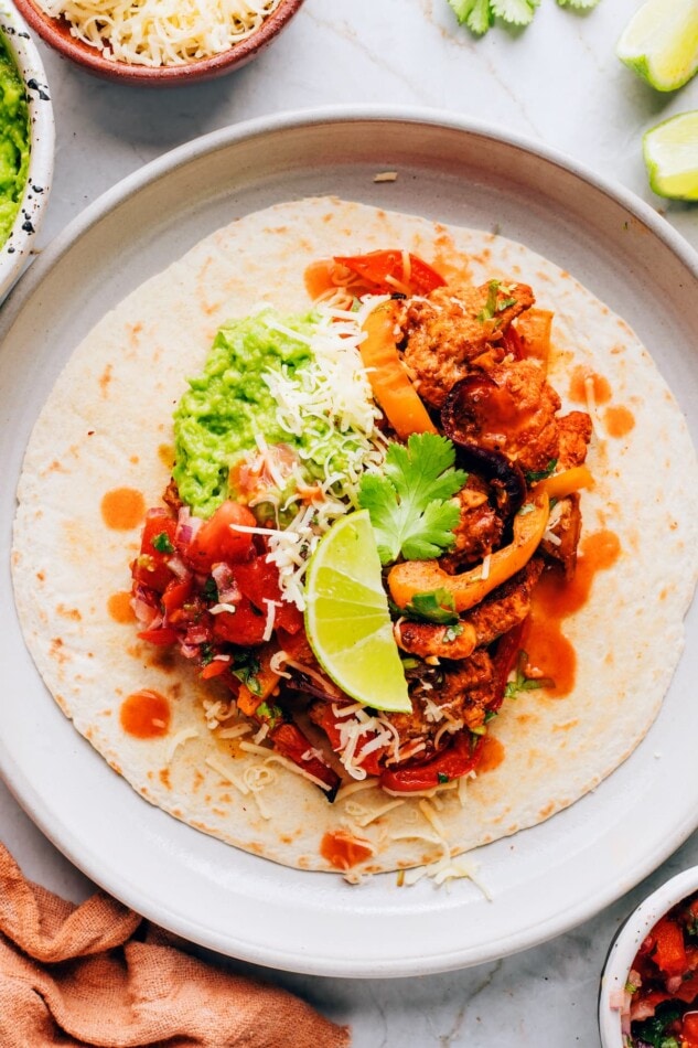 A tortilla on a plate topped with chicken fajita filling and a lime wedge.