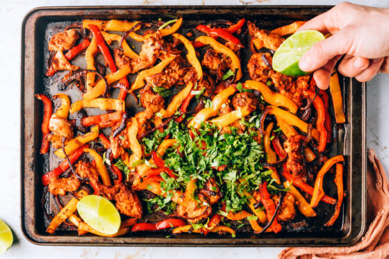 Cooked chicken fajita filling on a sheet pan garnished with parsley and a squeeze of lime.