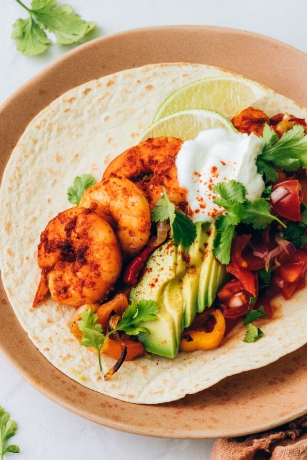 A shrimp fajita on a plate topped with avocado slices and greek yogurt.