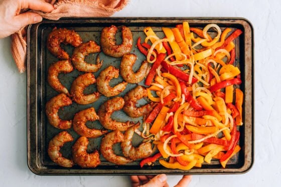 Cooked veggies on one half of a sheet pan with raw seasoned shrimp added to the other side.