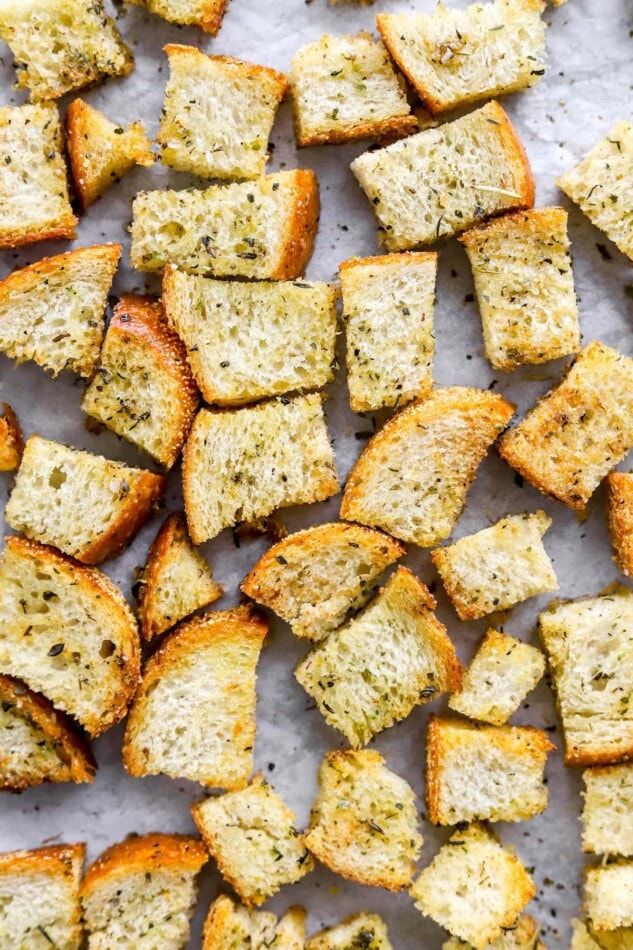 A closeup look at sourdough croutons on a baking sheet lined with parchment paper.