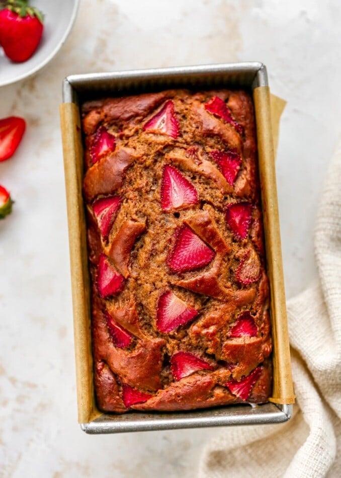 A loaf of strawberry banana bread in a bread pan lined with parchment paper.