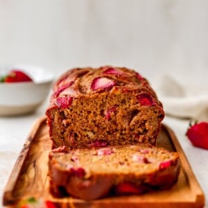 A loaf of strawberry banana bread, a slice has been cut and is resting next to the loaf.