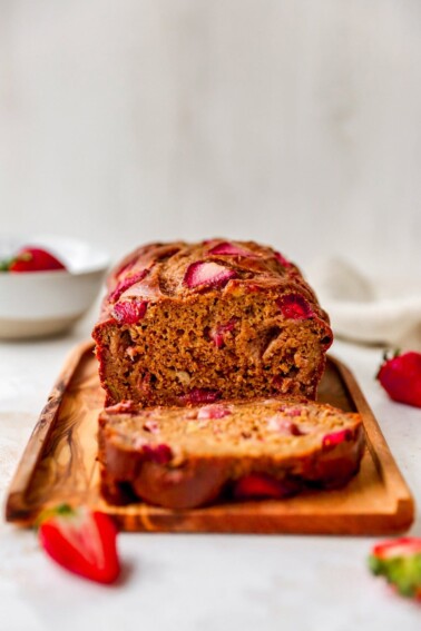 A loaf of strawberry banana bread, a slice has been cut and is resting next to the loaf.