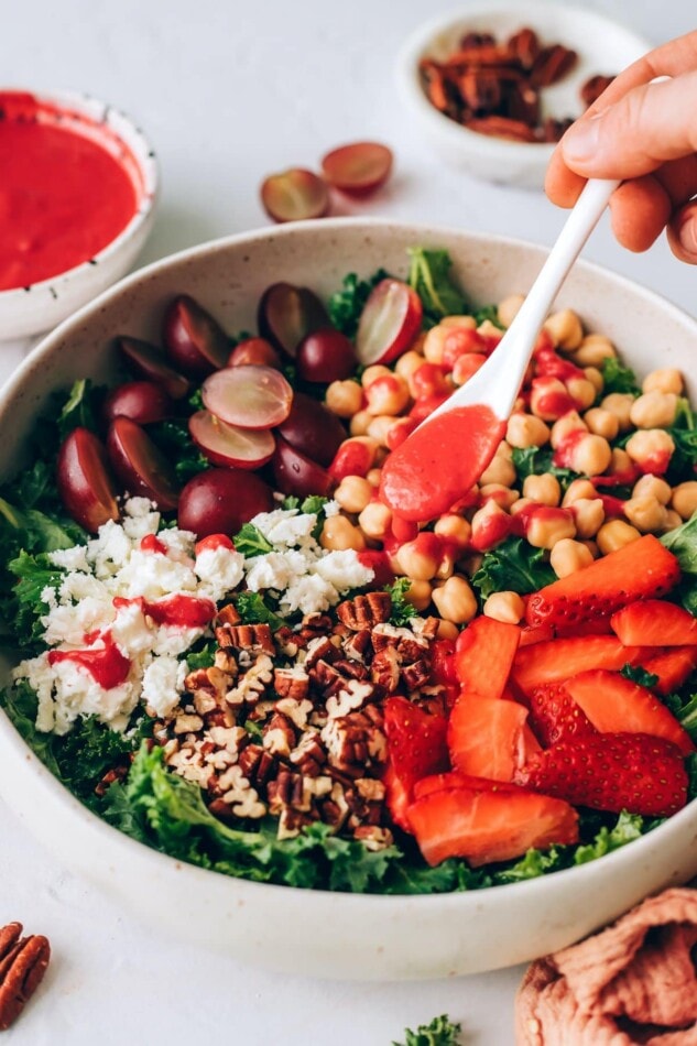 Drizzling raspberry vinaigrette onto a strawberry kale salad.