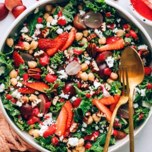A serving bowl with strawberry kale salad. Serving utensils rest in the bowl.