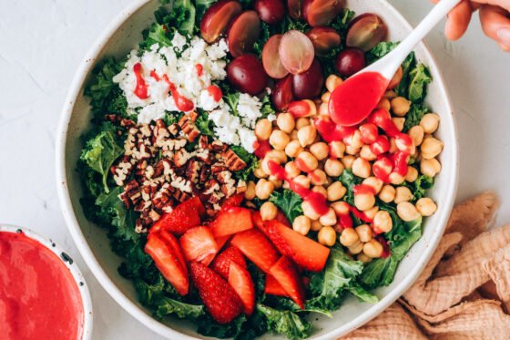 Drizzling raspberry vinaigrette over strawberry kale salad ingredients.