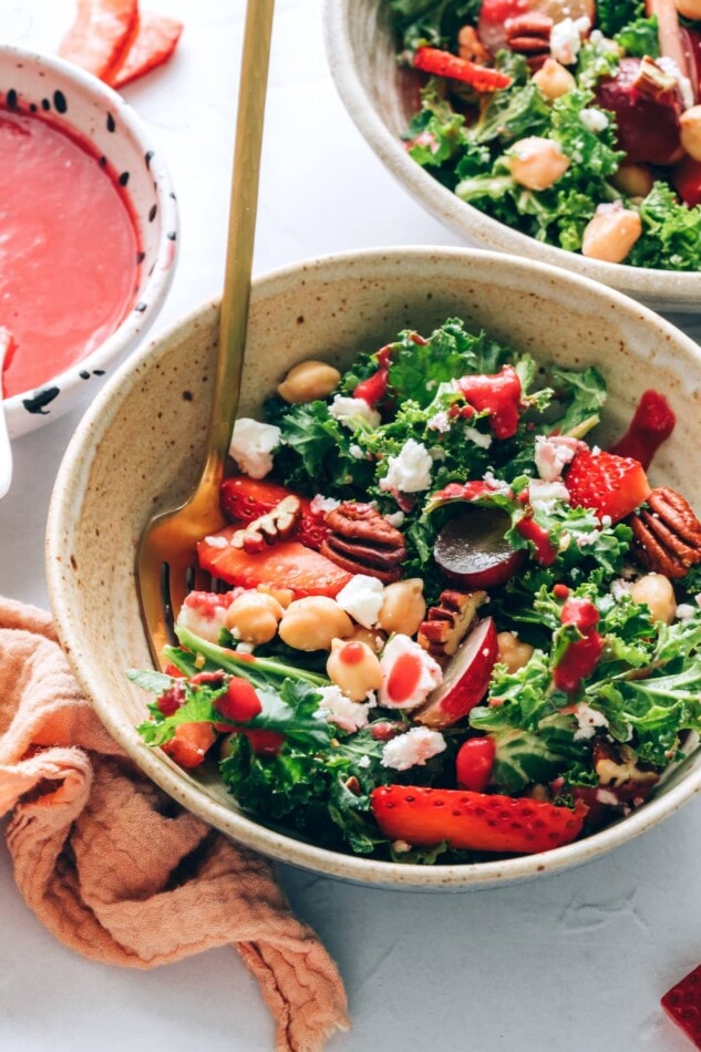 A bowl of strawberry kale salad with a fork resting in the bowl.