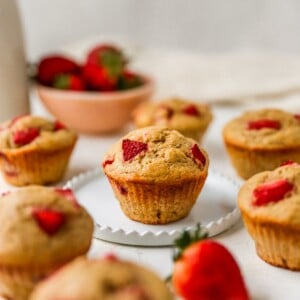 A muffin resting on a plate. The plate is surrounded by other muffins.