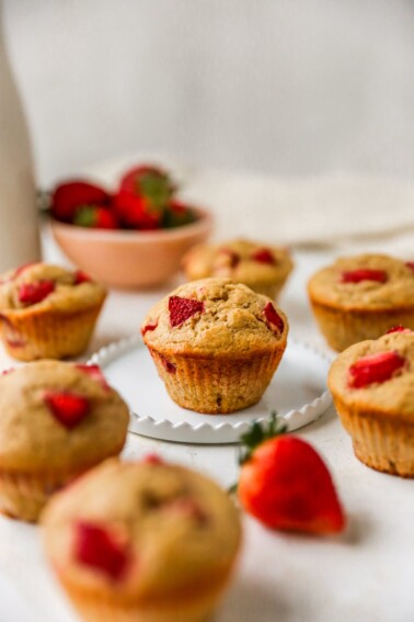 A muffin resting on a plate. The plate is surrounded by other muffins.