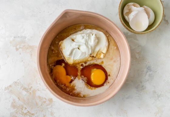 2 eggs, greek yogurt, oil, maple syrup, almond milk and vanilla extract in a bowl.